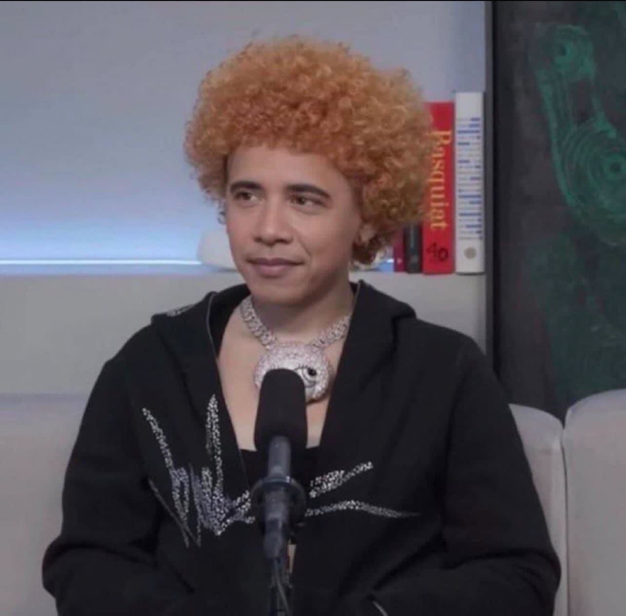 A person seated at a microphone with a patient look.